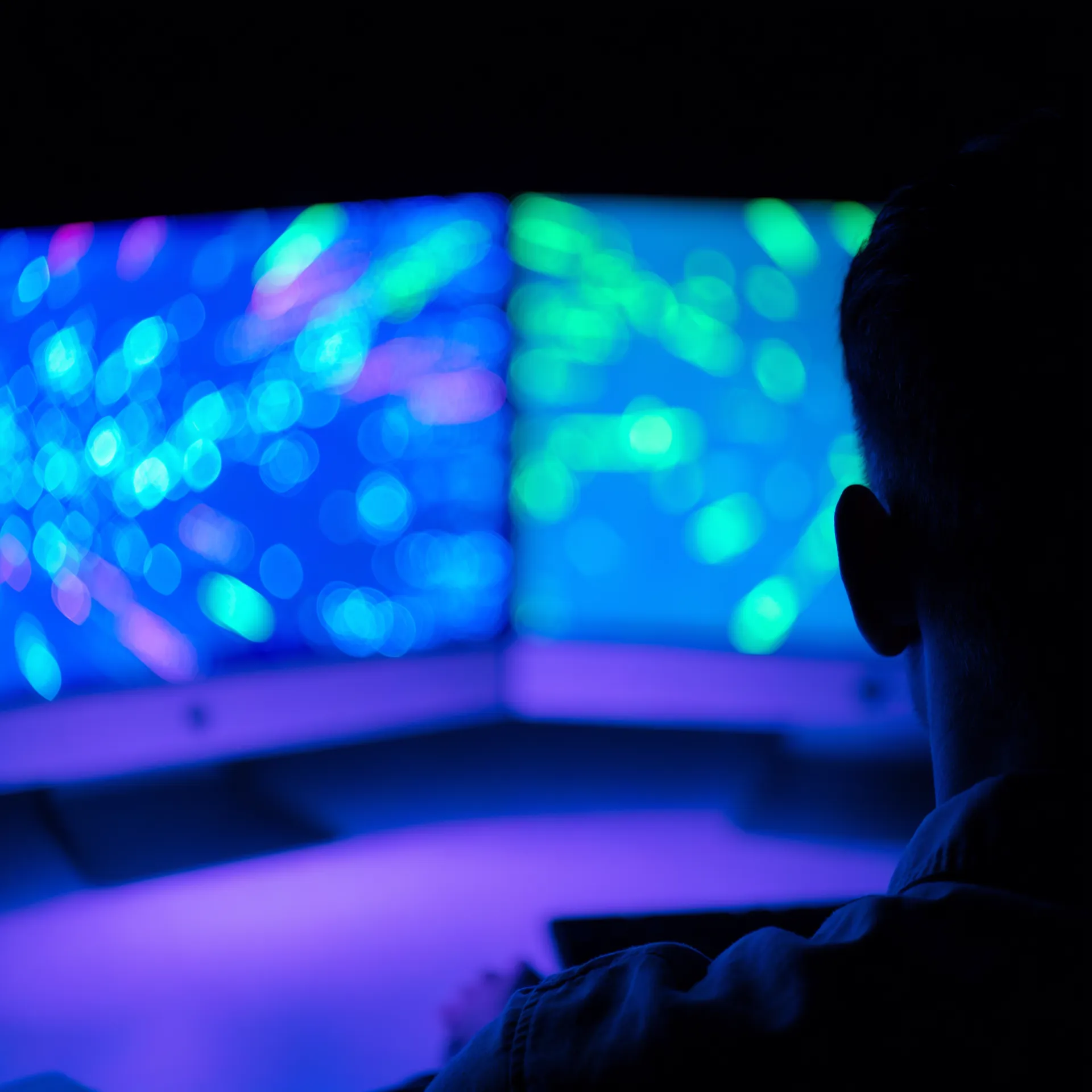 Engineer seen from behind working at two monitors glowing in blue and cyan