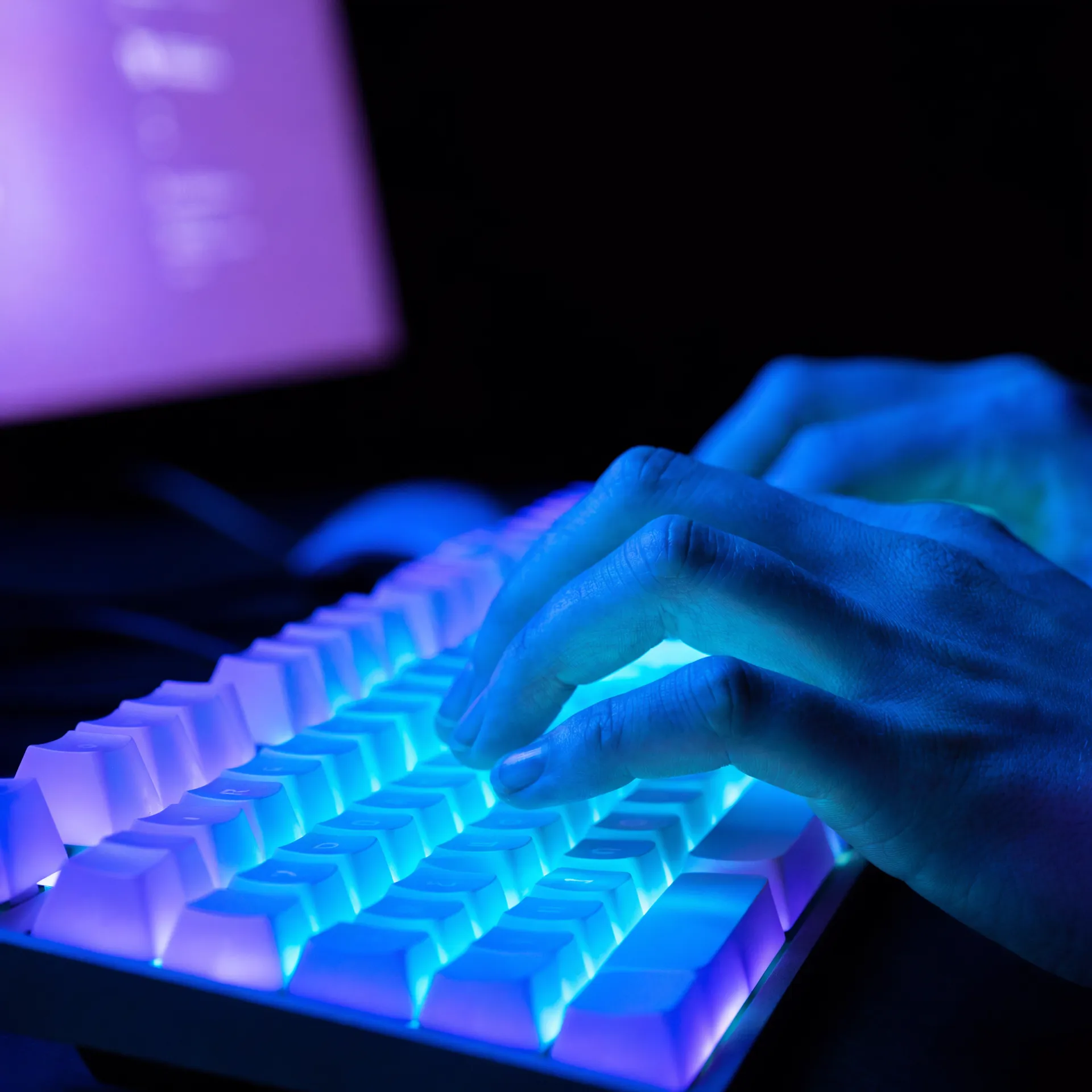 Hands typing on a backlit keyboard in a dark studio, lit in cobalt blue and cyan