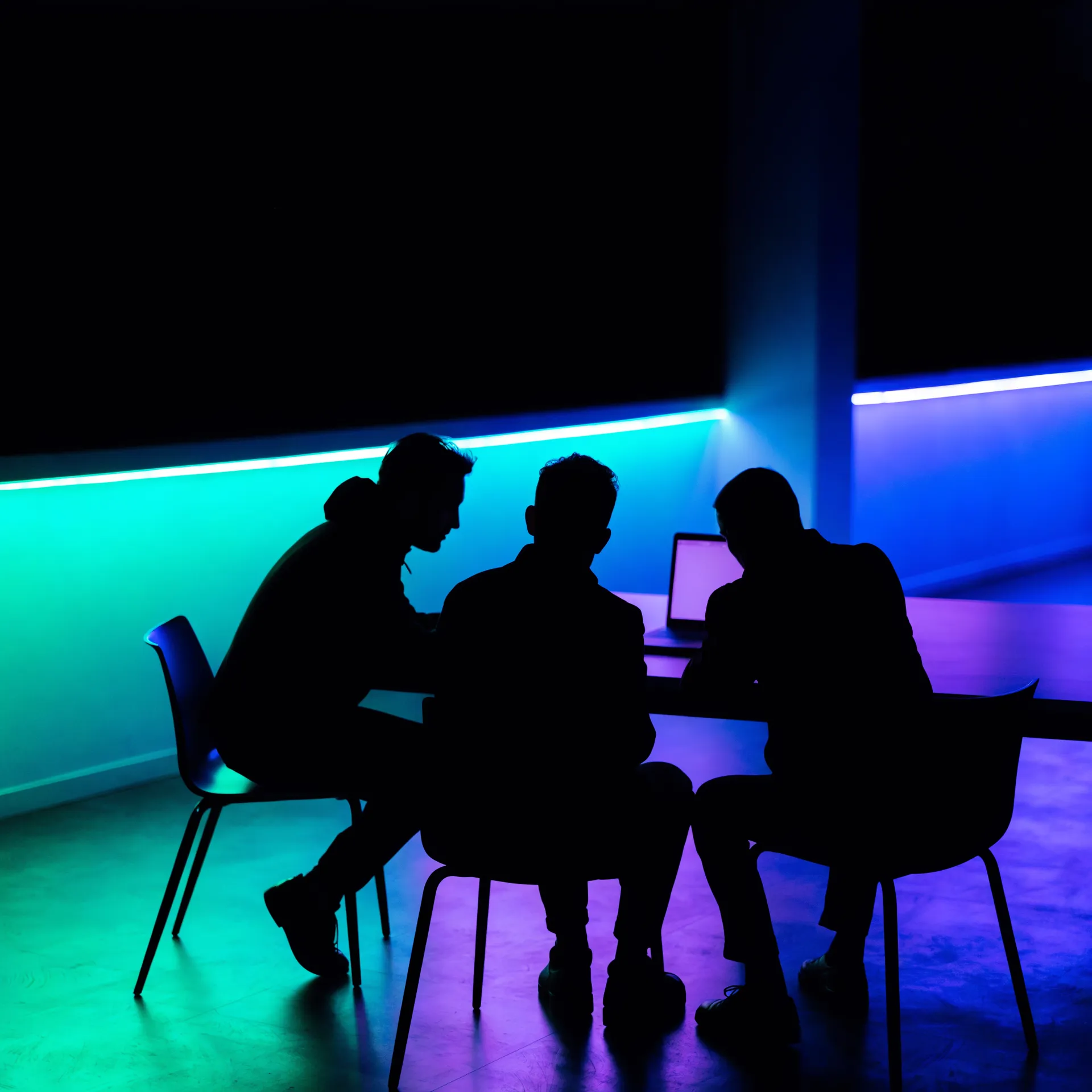 Three colleagues collaborating at a table as silhouettes under a cyan light strip